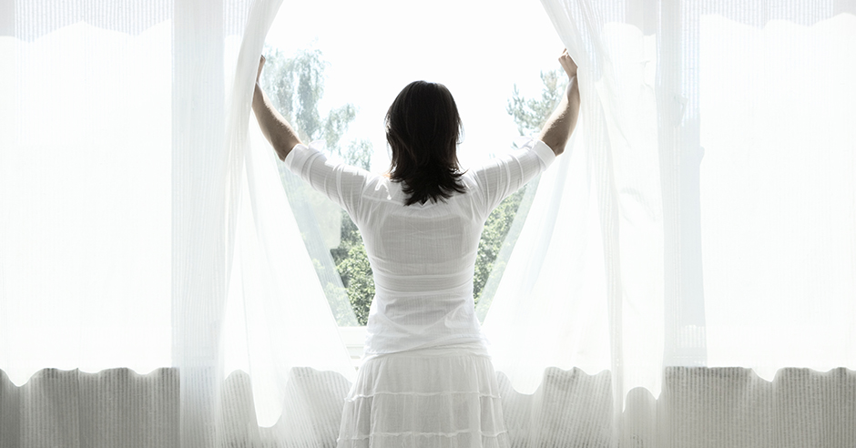Woman opening curtains, looking out window, rear view